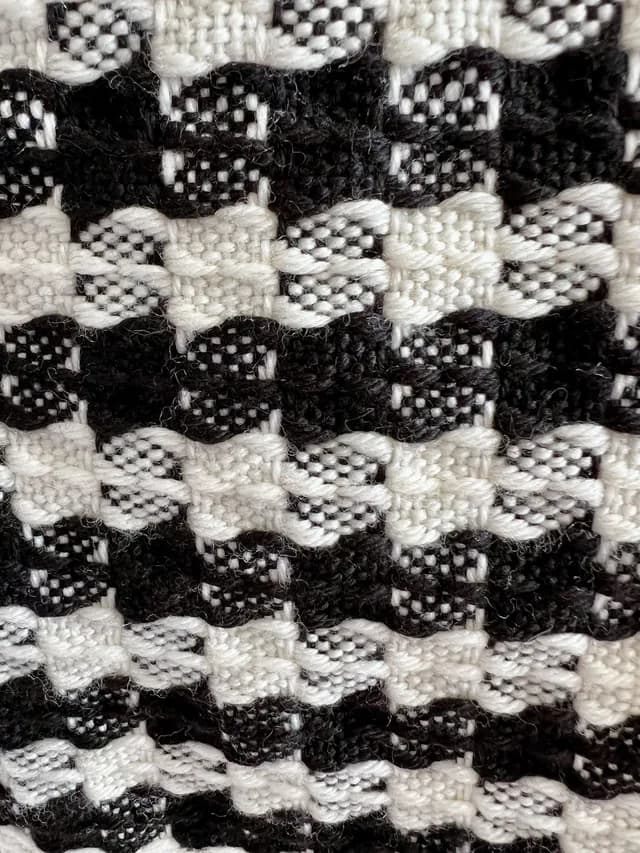 Gros plan sur le tissage texturé et le motif géométrique noir et blanc de l'écharpe en laine.
