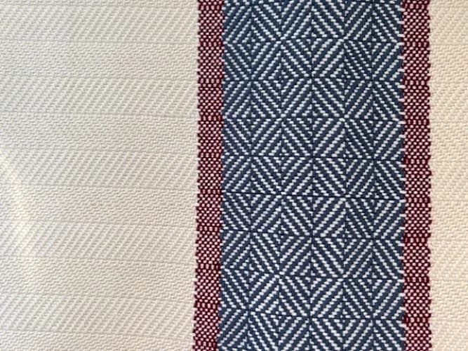 Détail du tissage à chevrons beige clair et de la bande géométrique bleue bordée de rouge.