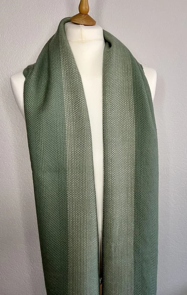 Écharpe verte tissée à motifs texturés drapée sur un mannequin de couture blanc.