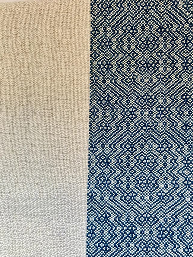 Détail du tissage d'une écharpe montrant un pan écru uni et un pan aux motifs géométriques bleus et blancs.
