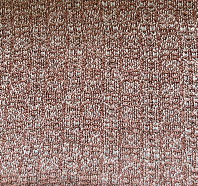 Gros plan sur le motif texturé du tissage artisanal aux teintes rosées et blanches.