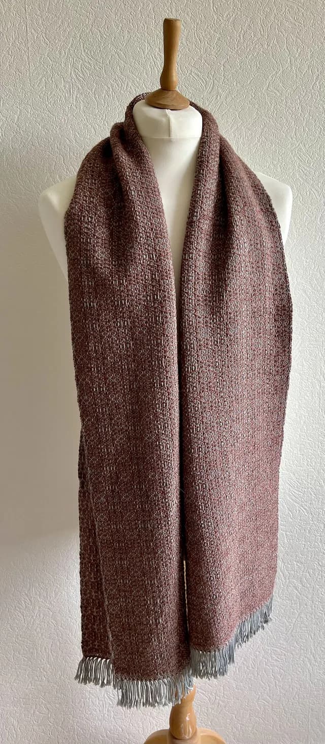 Écharpe tissée vieux rose et écru à franges portée sur un buste de mannequin blanc.