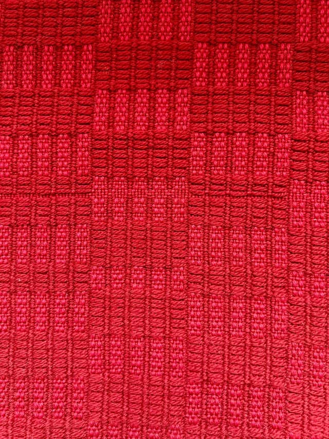 Gros plan sur le motif géométrique texturé du tissage en laine rouge.