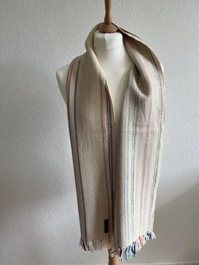 Écharpe tissée champagne à fines rayures colorées et franges, présentée sur un mannequin de couture.