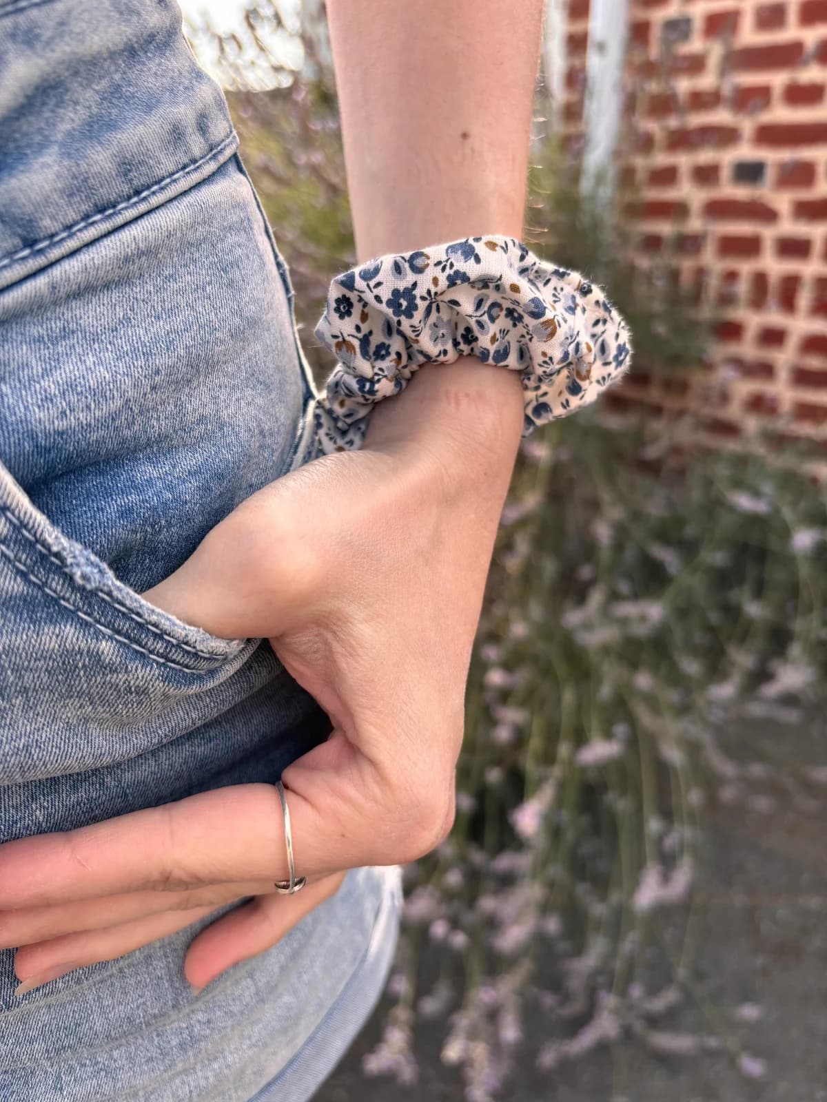 Chouchou en tissu écru à petites fleurs bleues porté au poignet devant un massif de lavande.