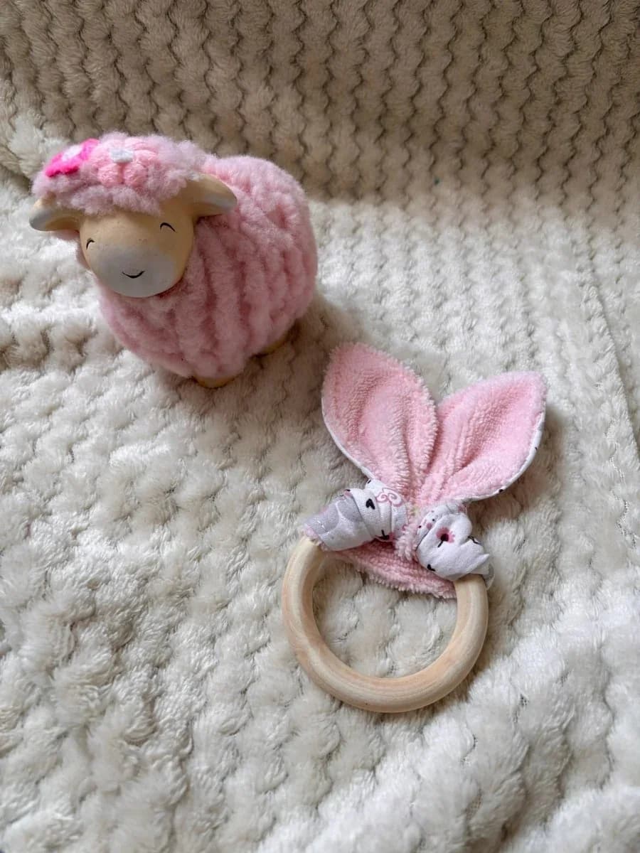 Petite main de bébé tenant l'anneau de dentition en bois avec tissu rose et blanc