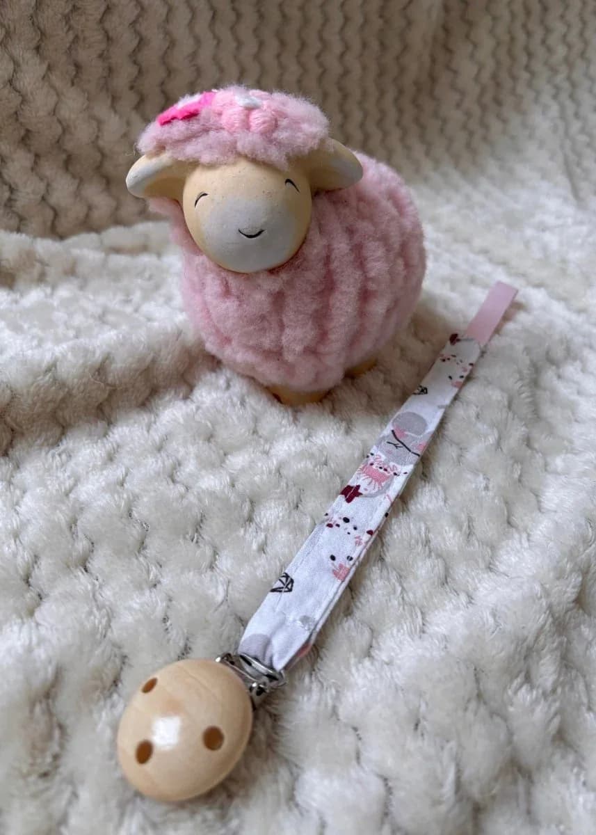 Bébé portant un gilet en tricot rose avec l'attache-tétine à motifs fixée à sa sucette.