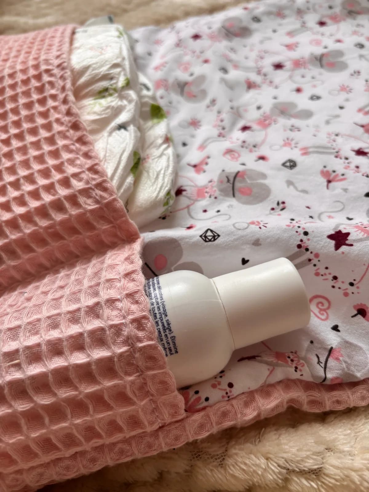 Vue d'ensemble du tapis à langer nomade rose et blanc aux motifs illustrés posé sur un plaid doux
