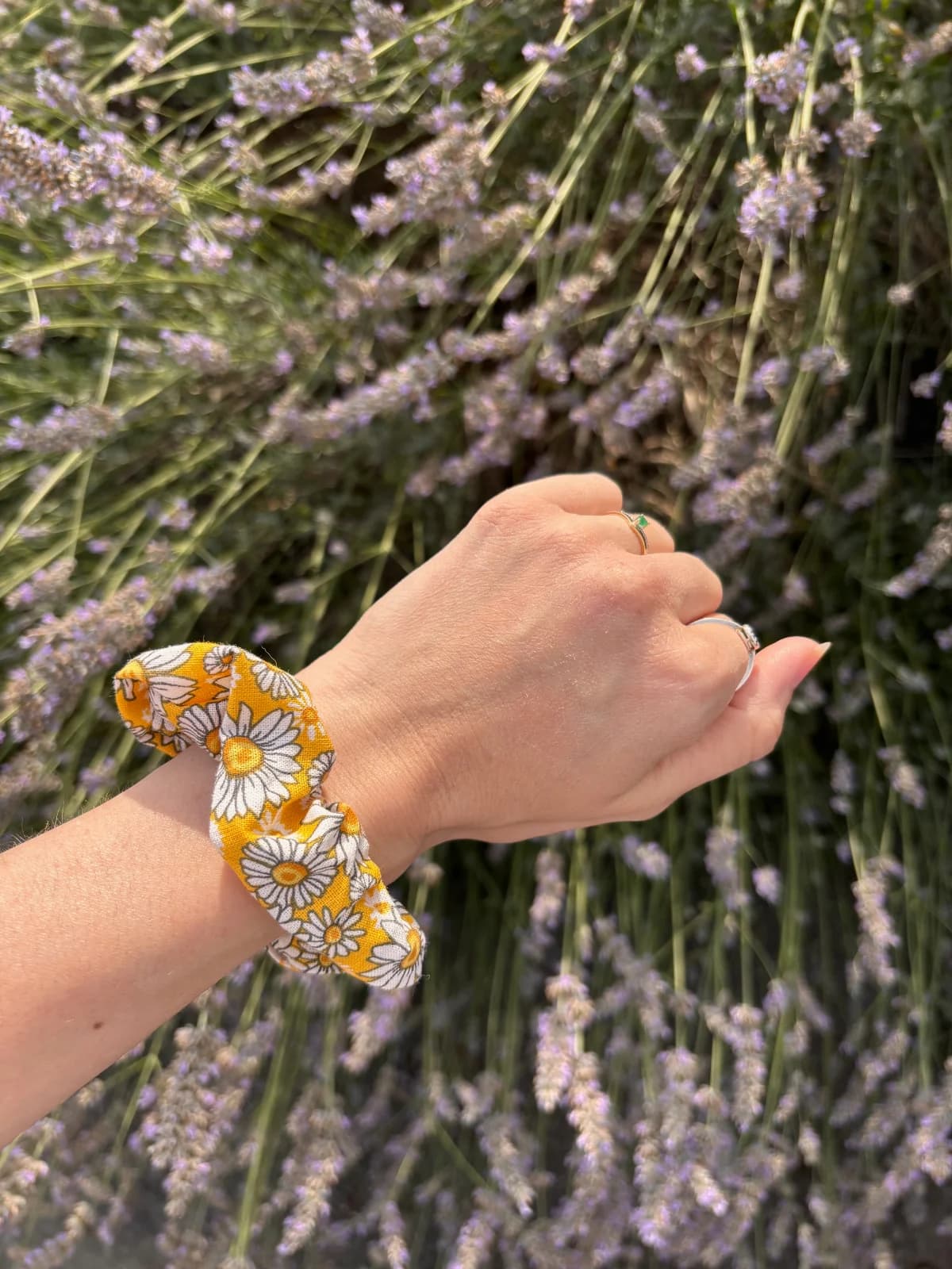 Élastique chouchou jaune à fleurs blanches porté au poignet devant des lavandes fleuries