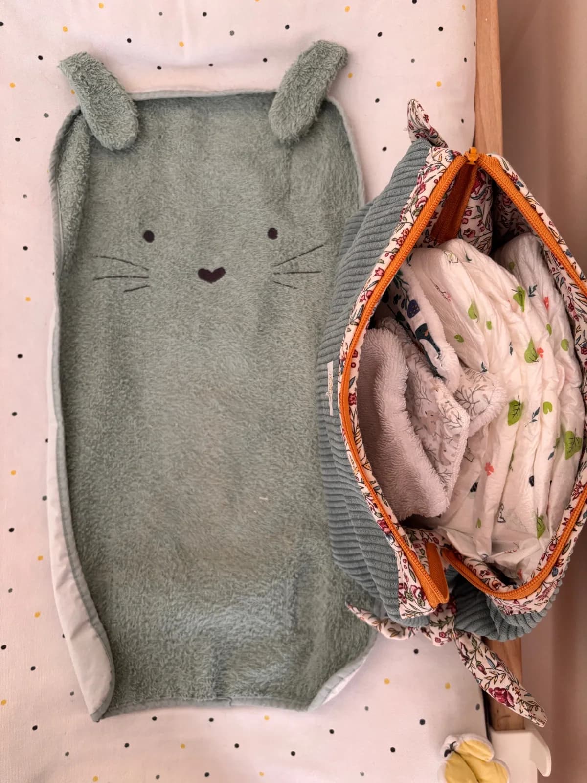 Trousse ouverte garnie de couches pour bébé, posée près d'un tapis à oreilles.