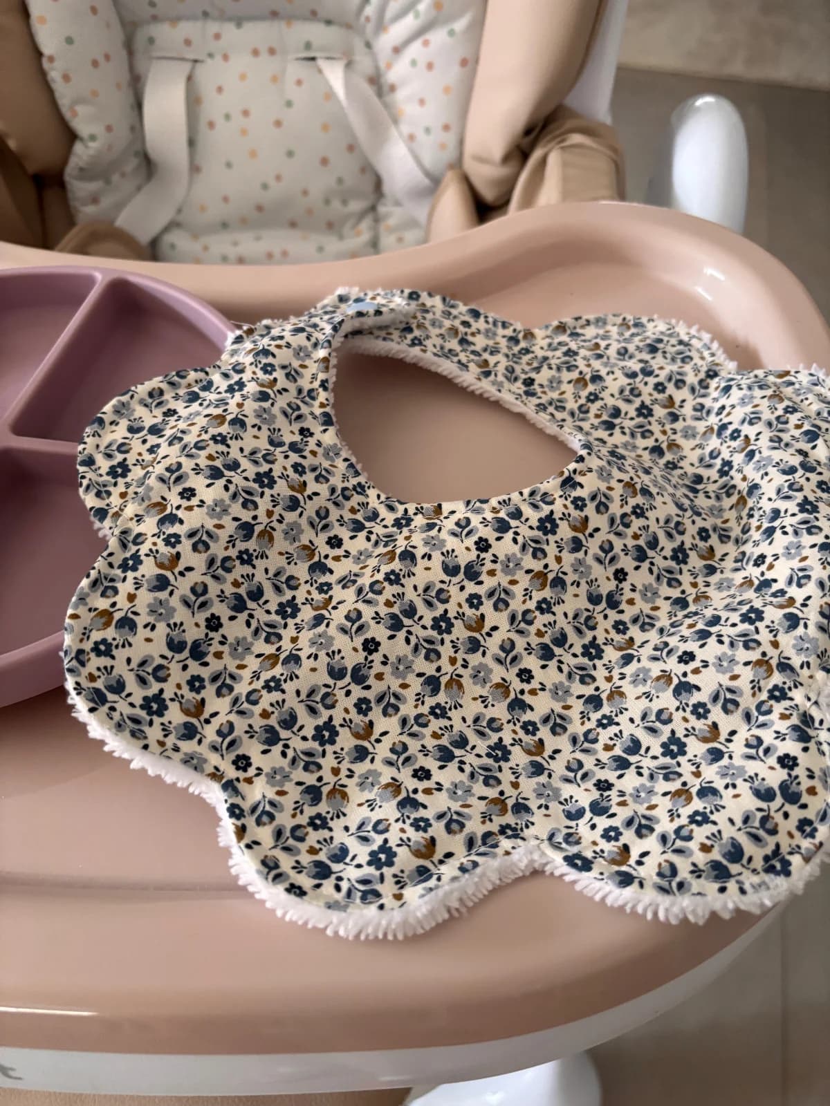 Bavoir fleur à motif fleuri bleu et doublure éponge blanche sur une tablette rose