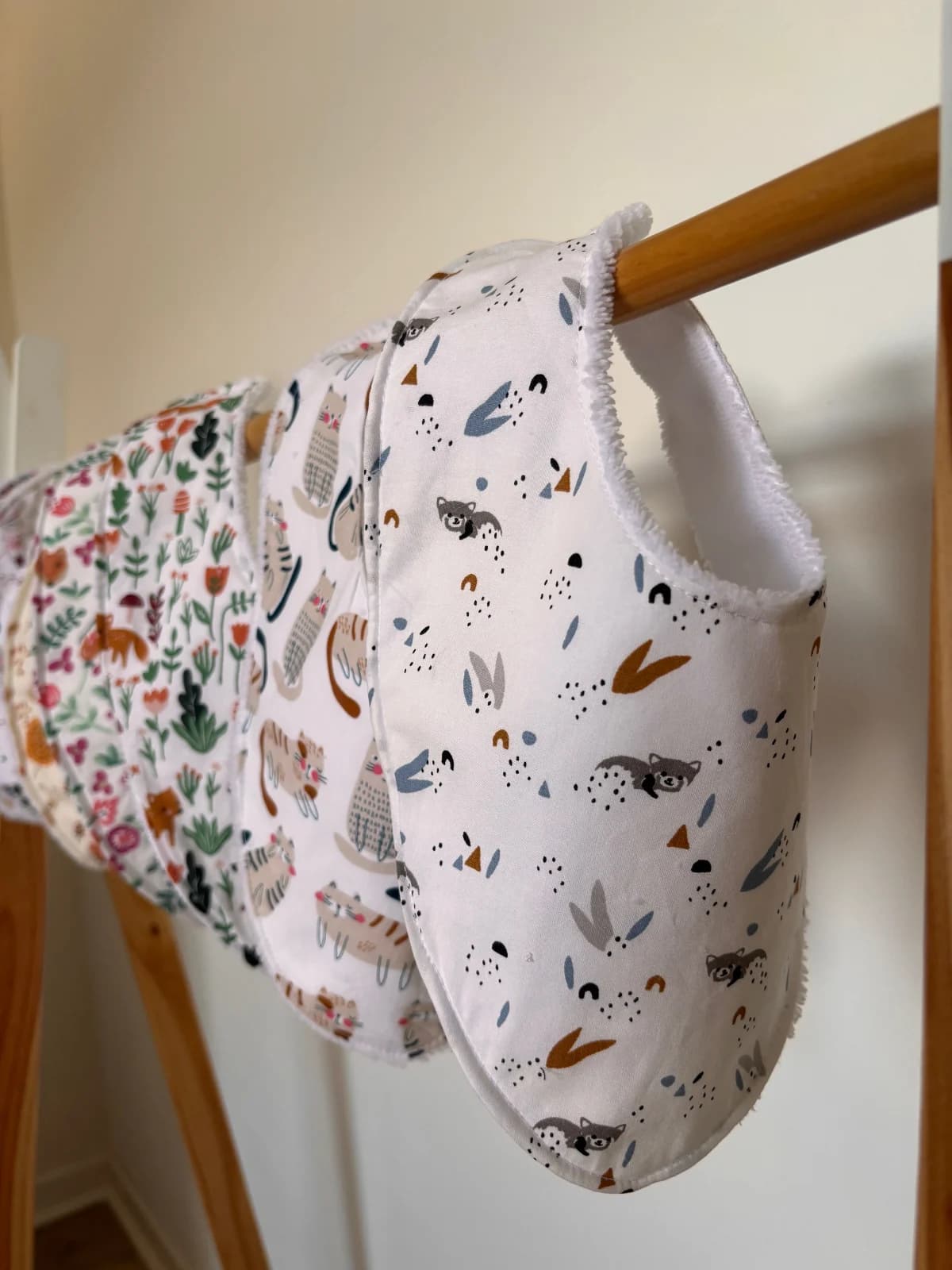 Bavoirs bandana à motifs d'animaux suspendus sur un portant en bois, doublés de tissu éponge blanc.