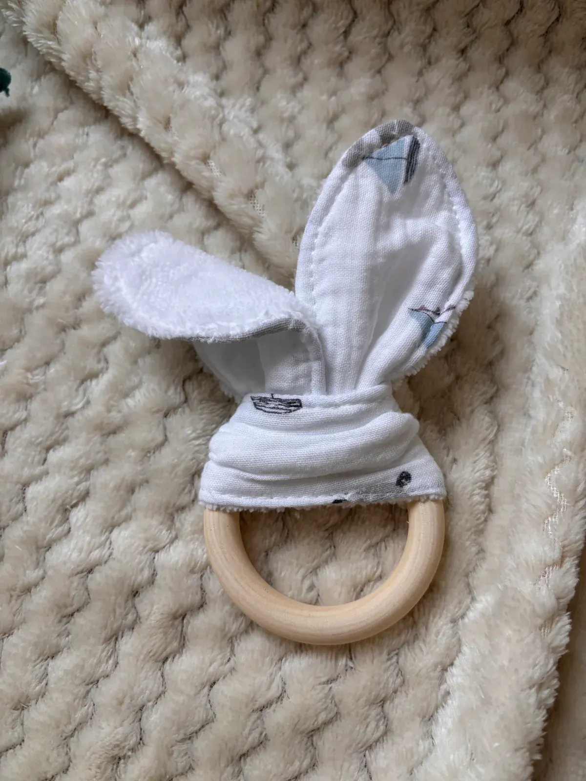 Anneau en bois naturel et tissu blanc à motifs oreilles de lapin posé à plat sur un plaid