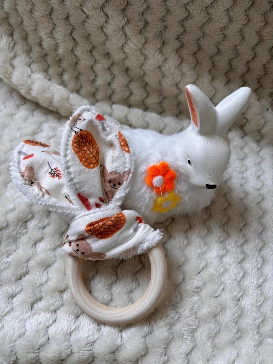 Anneau de dentition en bois et tissu à motif automnal posé à côté d'une figurine de lapin blanc.