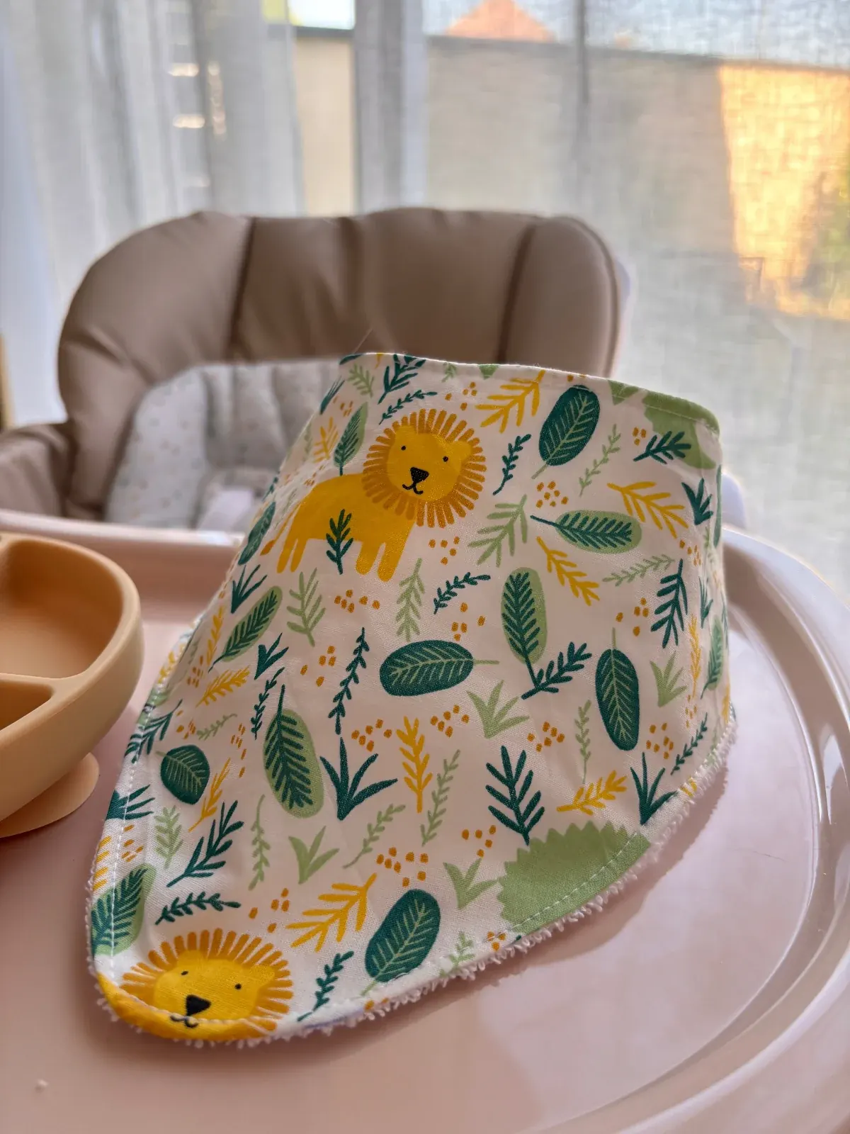 Bavoir bandana jungle tropicale blanc à motifs lion et feuillage vert posé sur une chaise haute