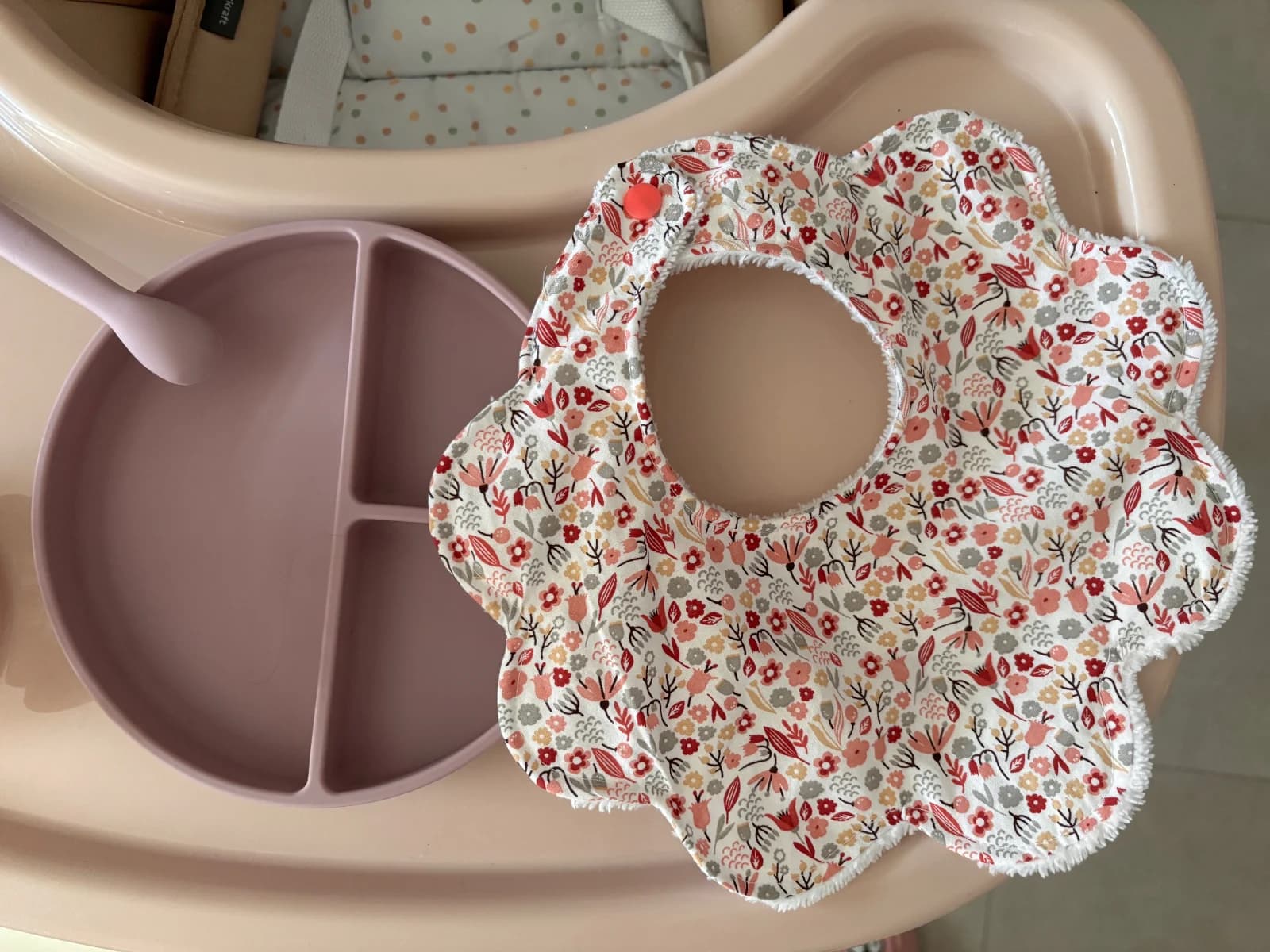 Bavoir en forme de fleur à motif fleuri posé sur une tablette à côté d'une assiette pour bébé
