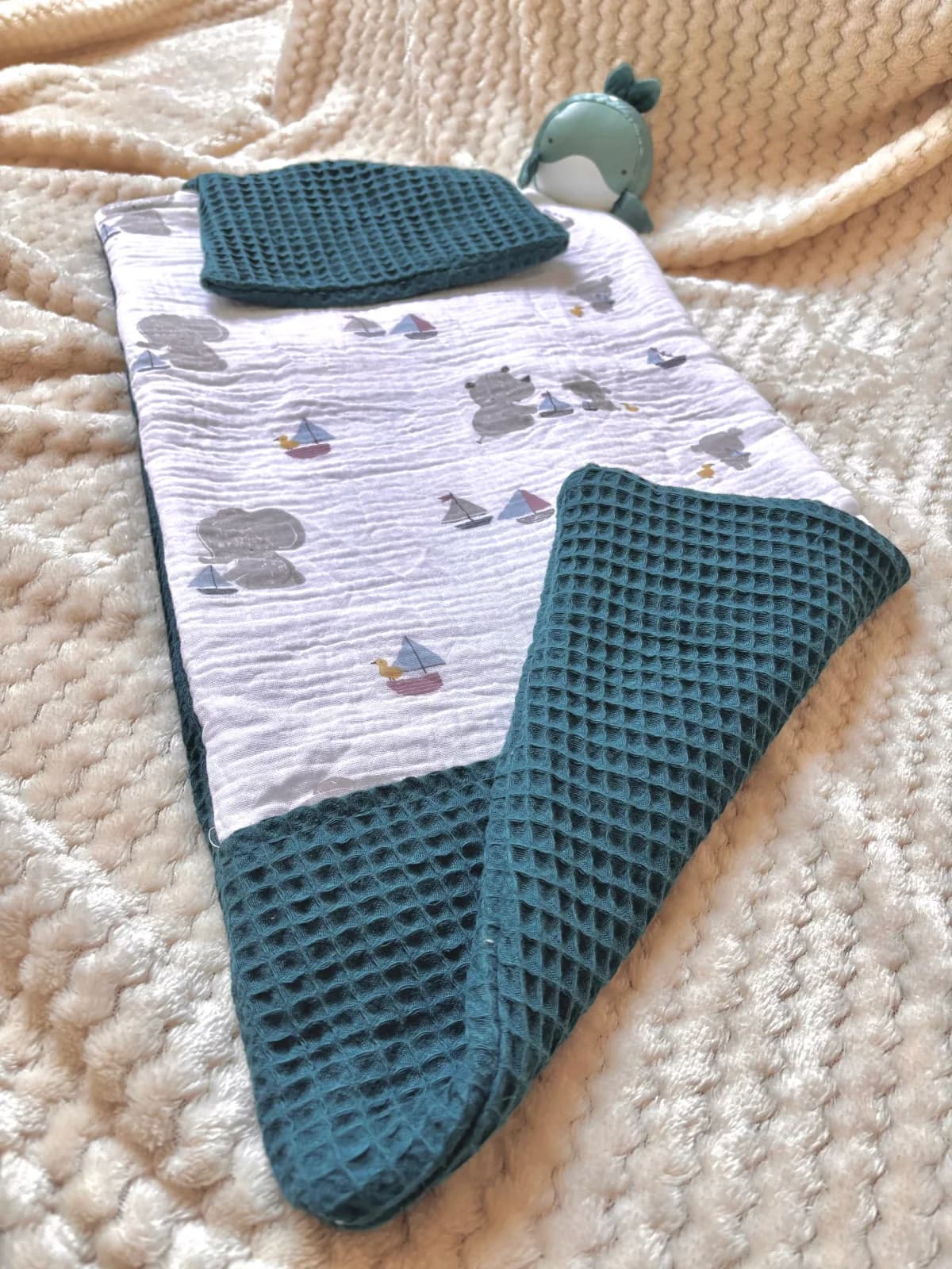 Vue oblique du matelas à langer avec rabat en nid d'abeille bleu canard sur couverture beige