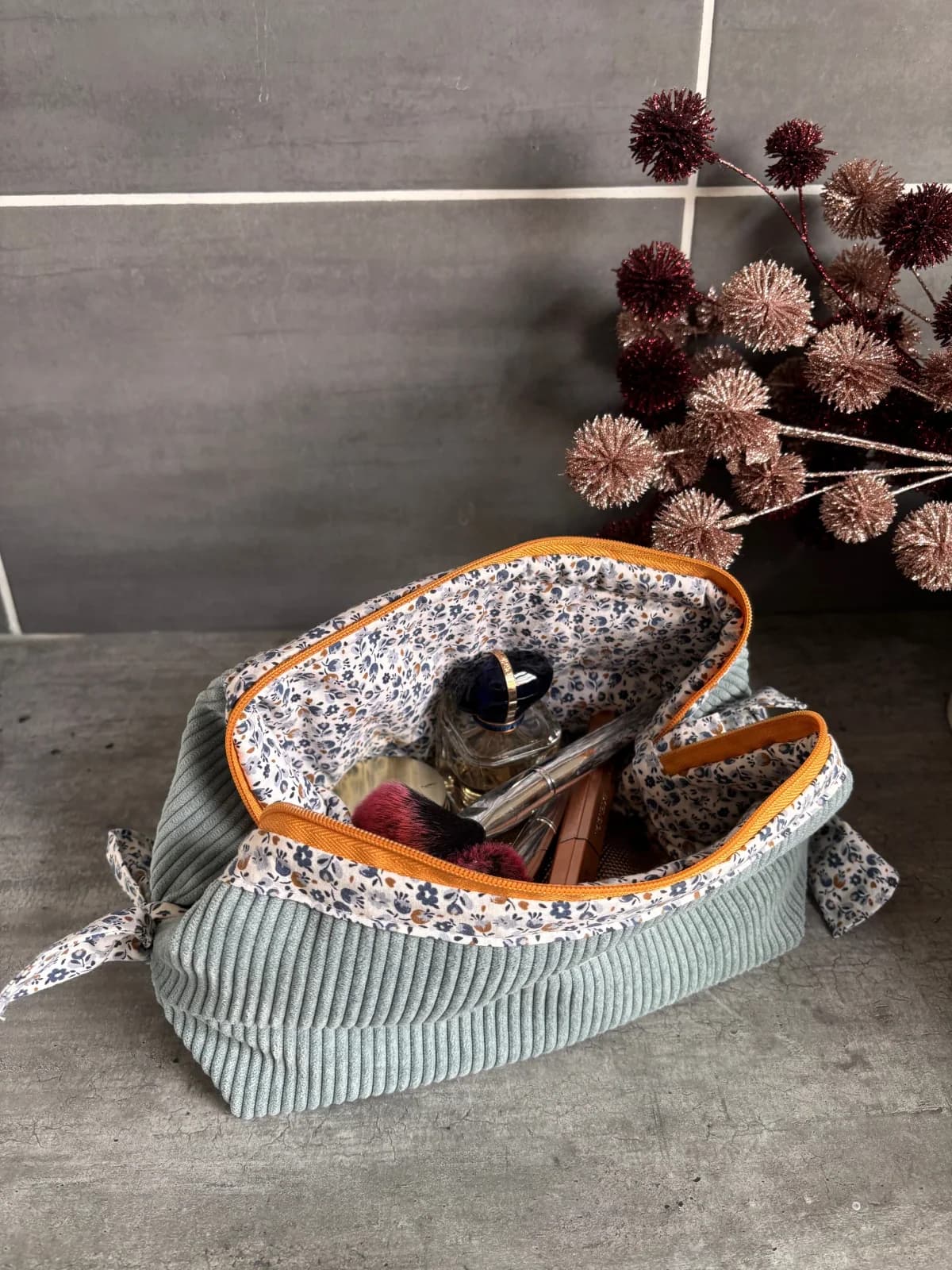 Trousse ouverte garnie de maquillage et parfum, dévoilant sa doublure intérieure à motifs fleuris.