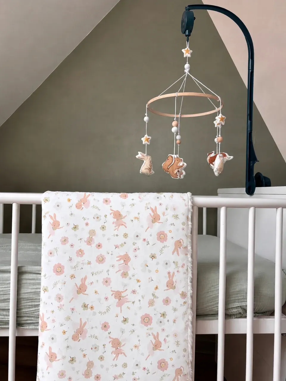Couverture bébé à motifs floraux et lapins roses suspendue aux barreaux d'un lit d'enfant.