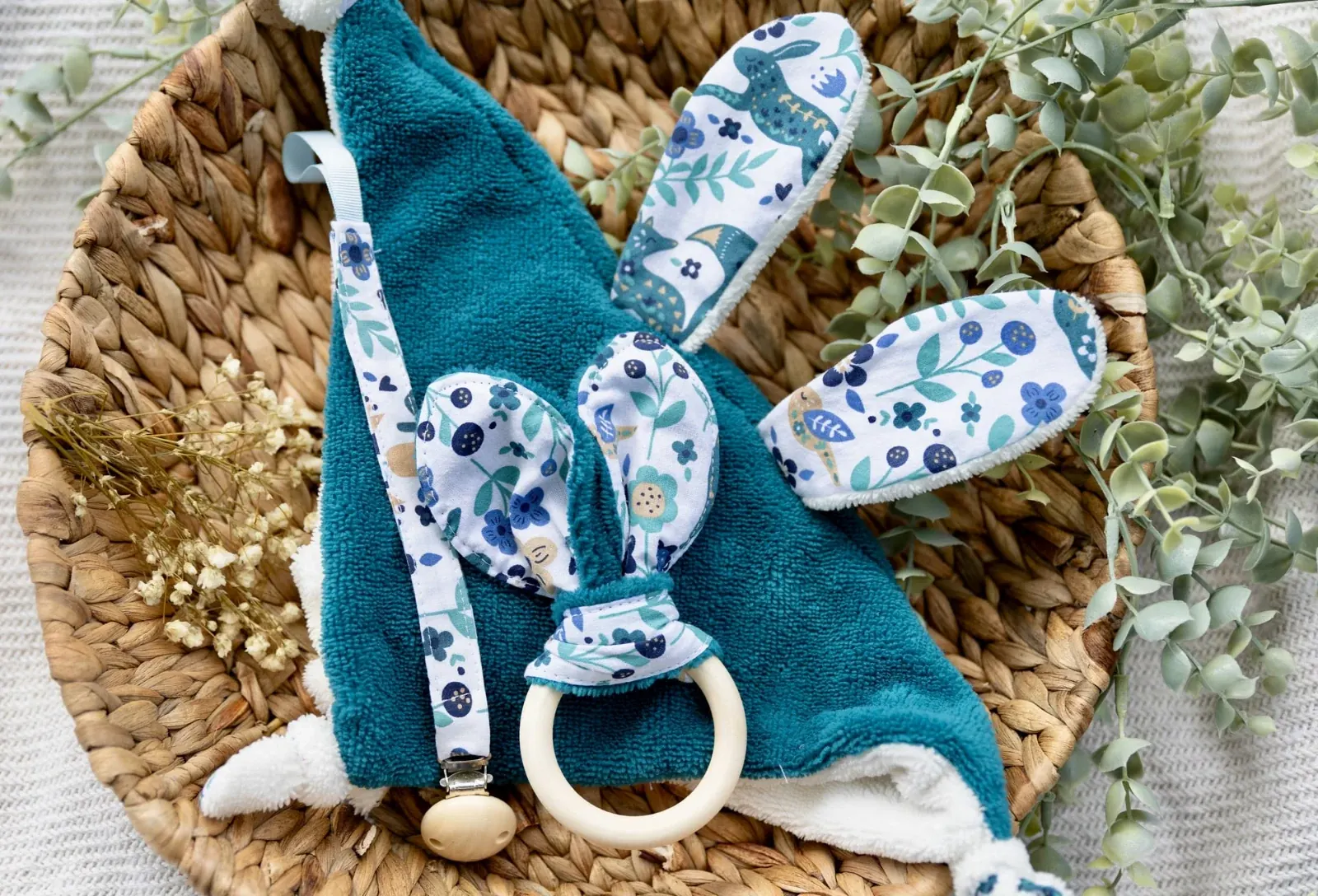 Doudou plat lapin bleu canard, attache-tétine et anneau de dentition dans une corbeille