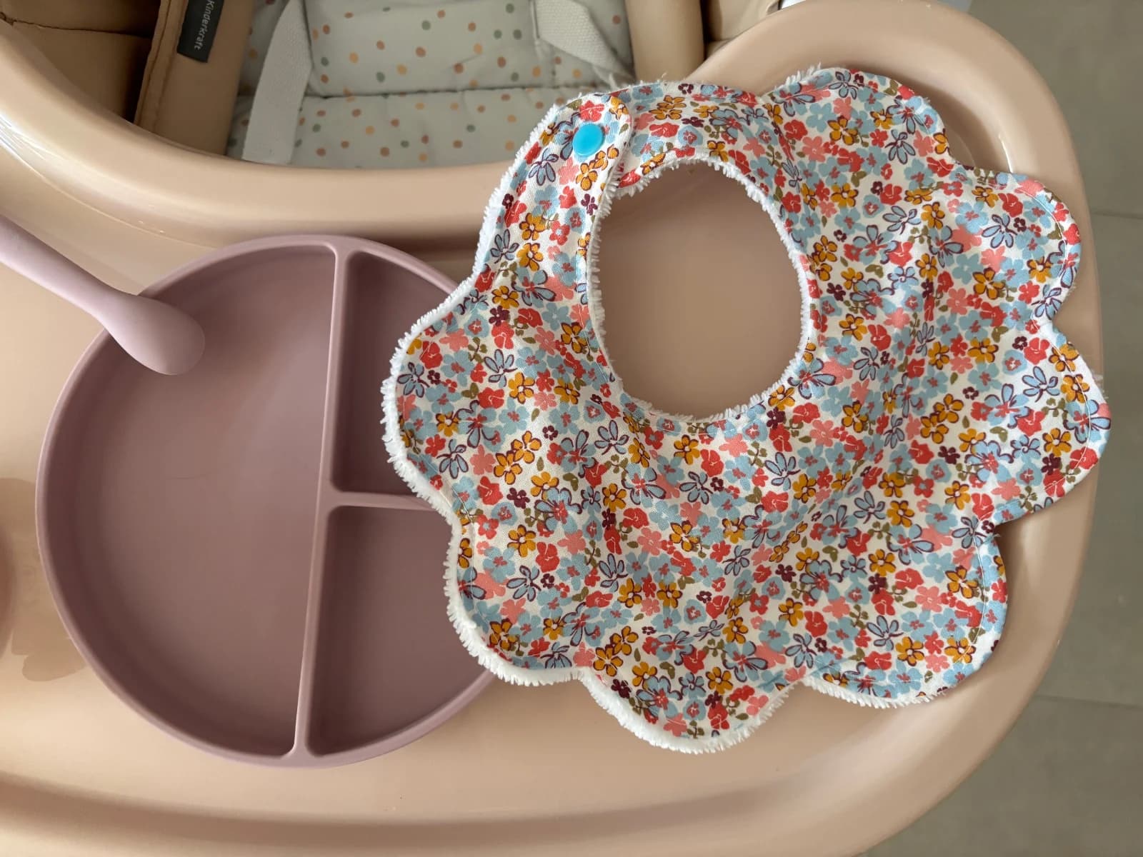 Bavoir en forme de fleur à motif floral multicolore posé sur un plateau de chaise haute avec une assiette