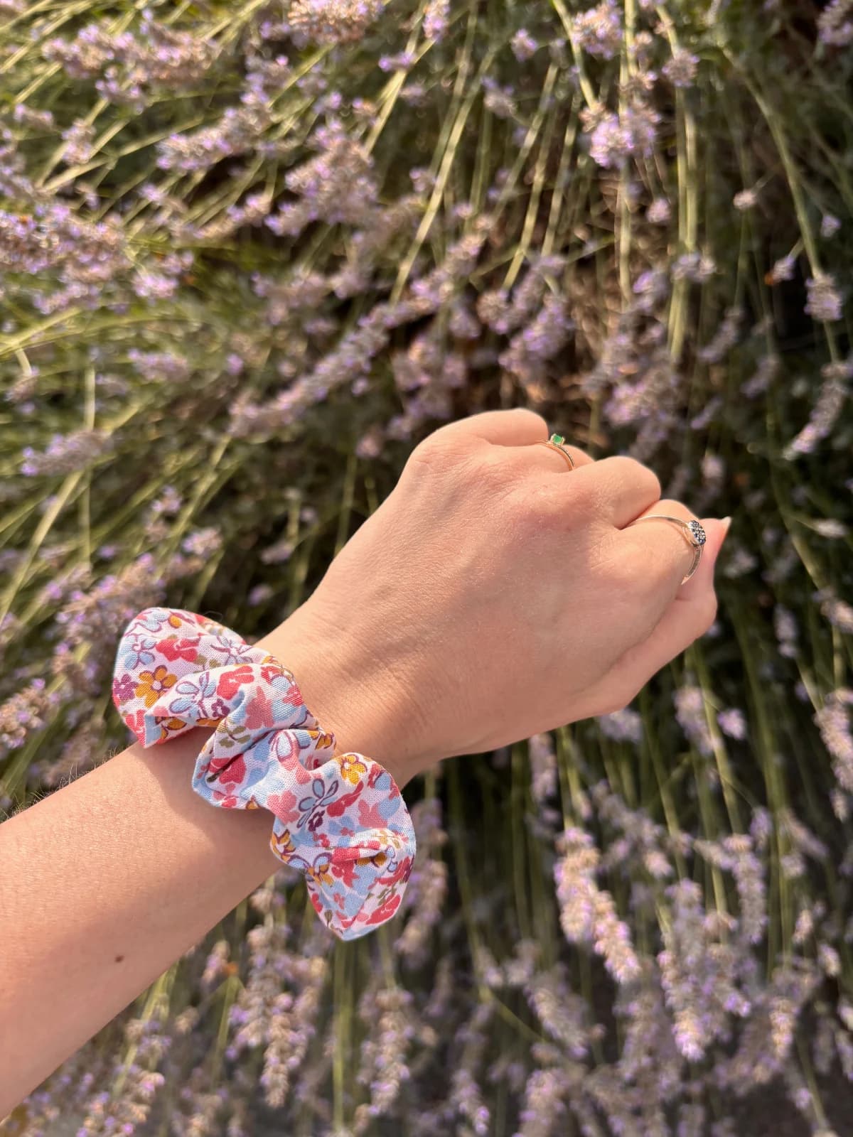 Gros plan sur le chouchou à motifs fleuris pastel porté au poignet devant des fleurs de lavande
