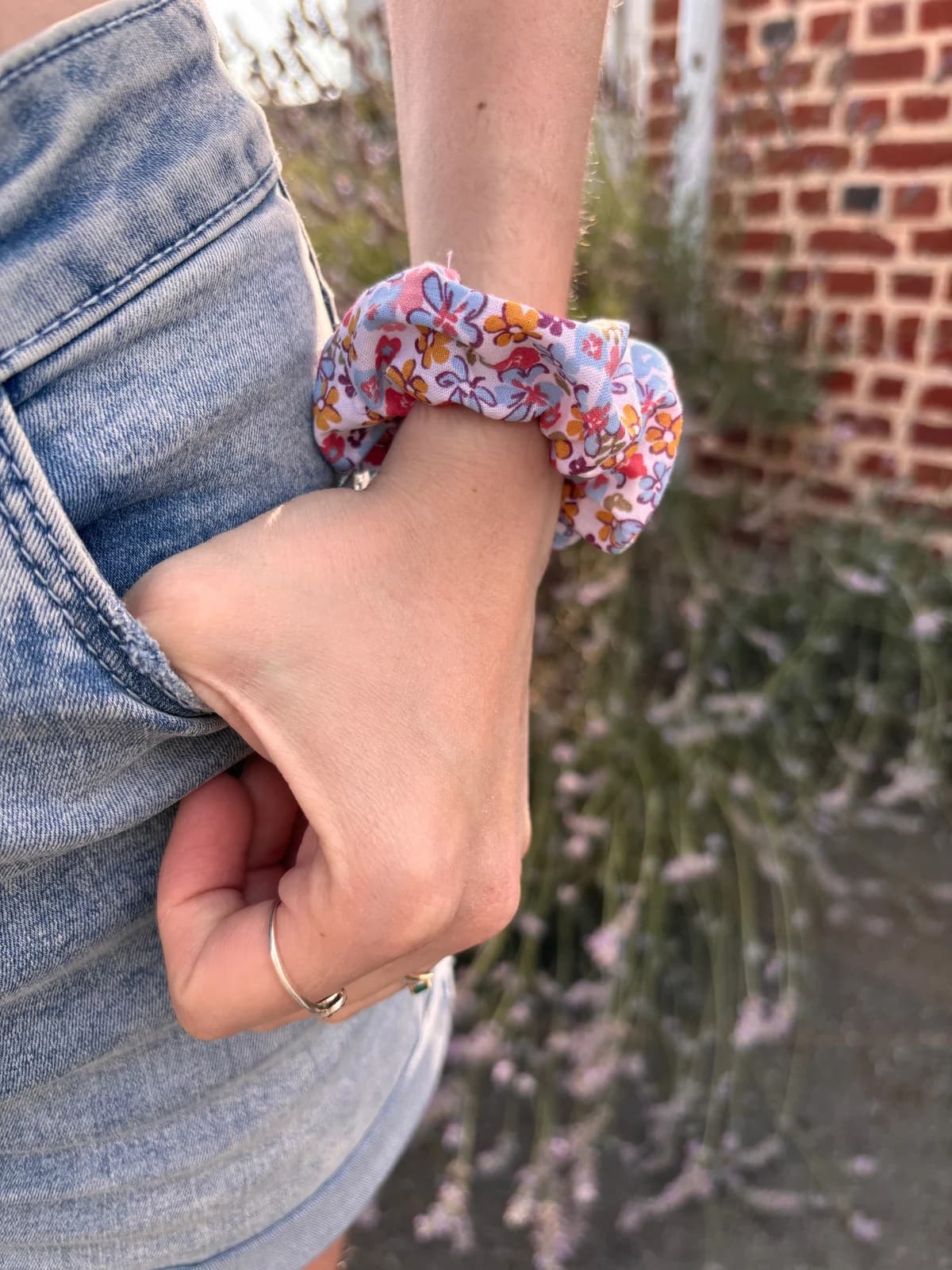 Chouchou fleuri rose, bleu et jaune porté au poignet d'une personne la main dans la poche
