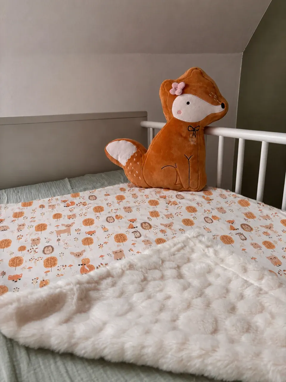 Couverture pour bébé pliée sur un panier en osier montrant son tissu imprimé automnal et sa polaire texturée.