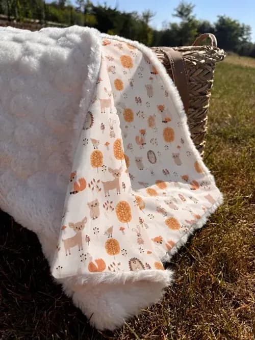 Couverture à motifs d'animaux des bois et revers en polaire écru posée sur un lit près d'un coussin renard.