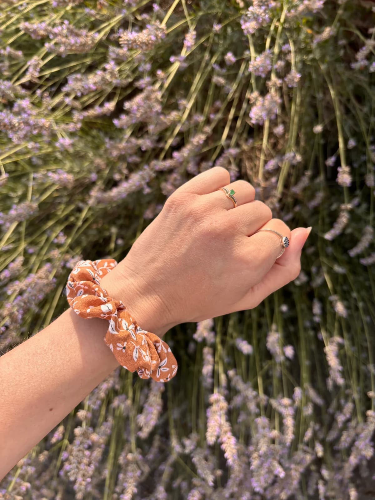 Chouchou couleur cannelle à motifs végétaux porté au poignet, devant des fleurs de lavande.
