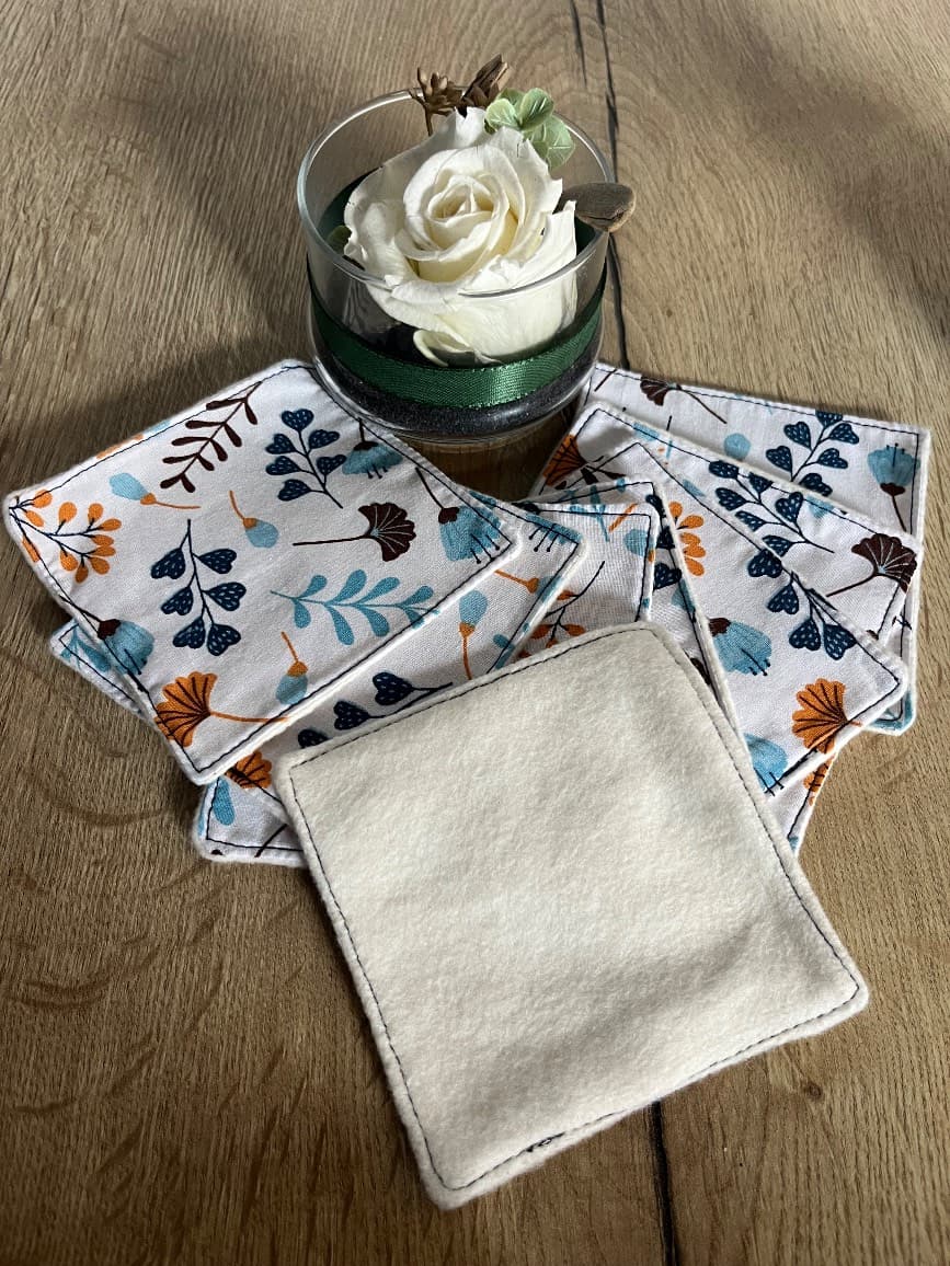 Ensemble de lingettes carrées à motifs floraux et face claire, étalées sur une table en bois.