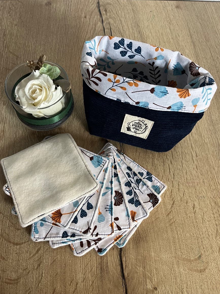 Panier en tissu bleu marine avec ses lingettes carrées à motifs floraux disposées en éventail sur une table.