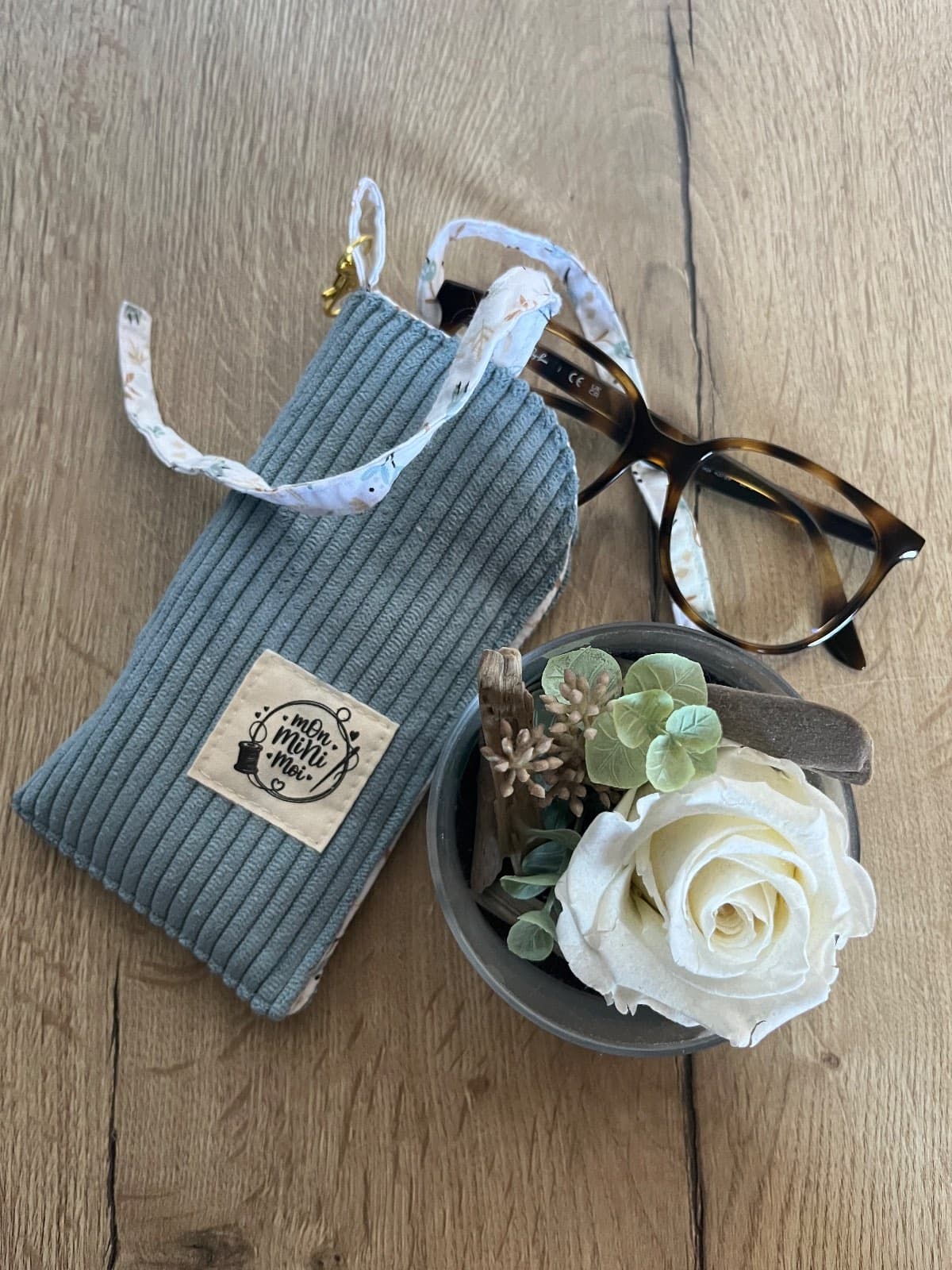 Pochette à lunettes en velours côtelé bleu jean avec attache mousqueton doré et finitions fleuries.