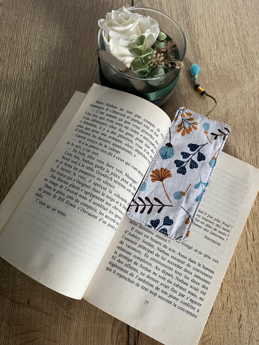 Marque-page en tissu à motifs feuillage bleu et moutarde placé dans les pages d'un livre ouvert.