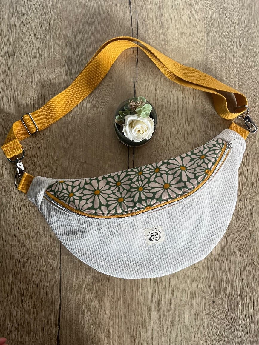Sac banane en velours côtelé blanc crème à motif fleuri et sangle jaune moutarde posé sur une table.