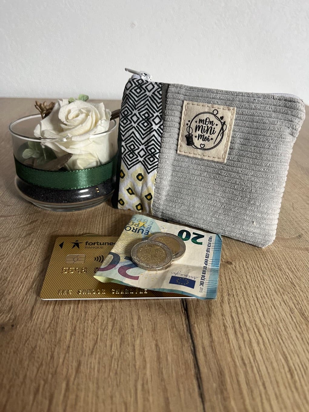 Porte-monnaie zippé en velours côtelé gris et tissu géométrique avec pièces et carte bancaire.