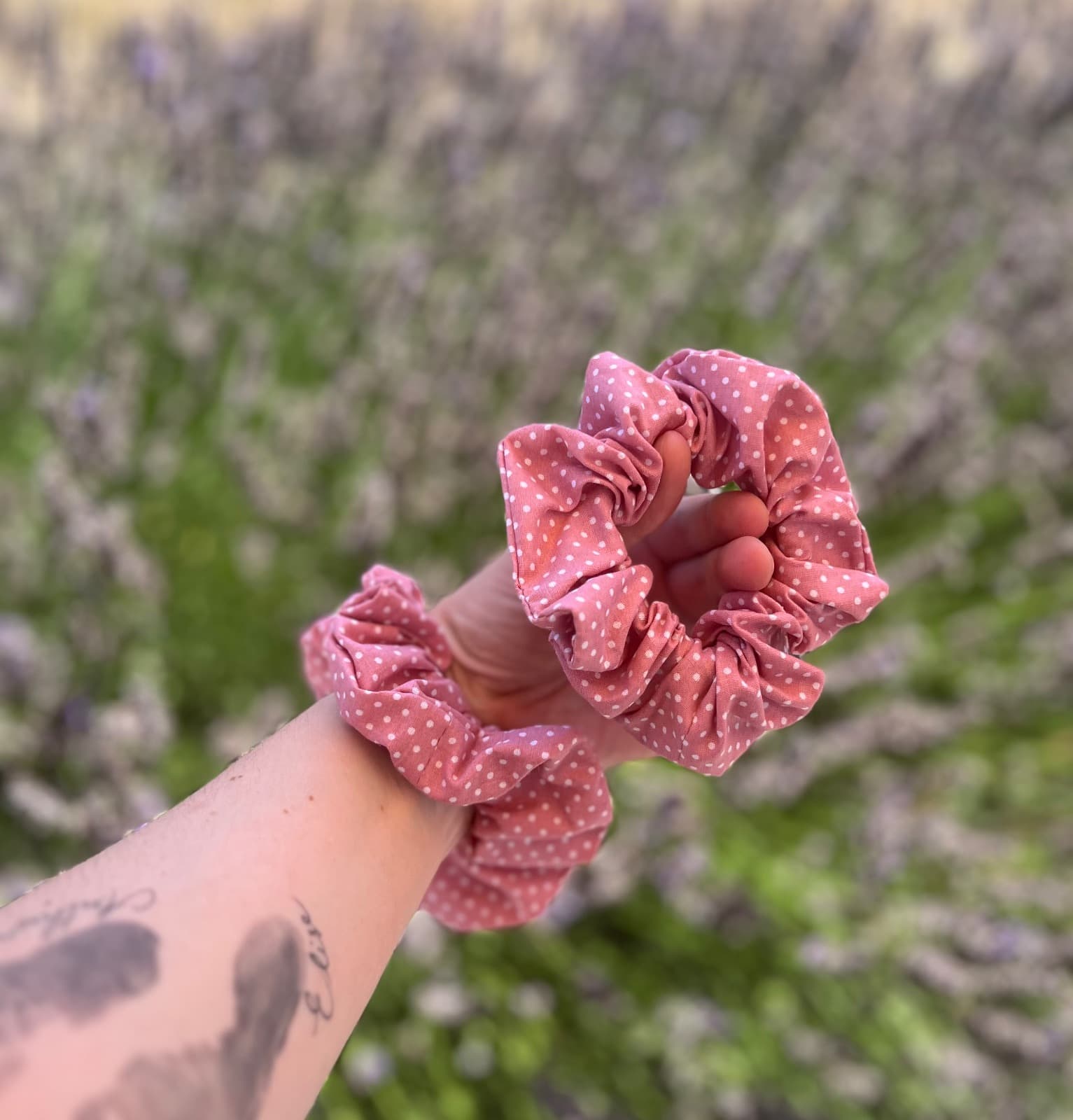 Chouchous en tissu rose à pois blancs présentés au poignet et dans la main en extérieur.