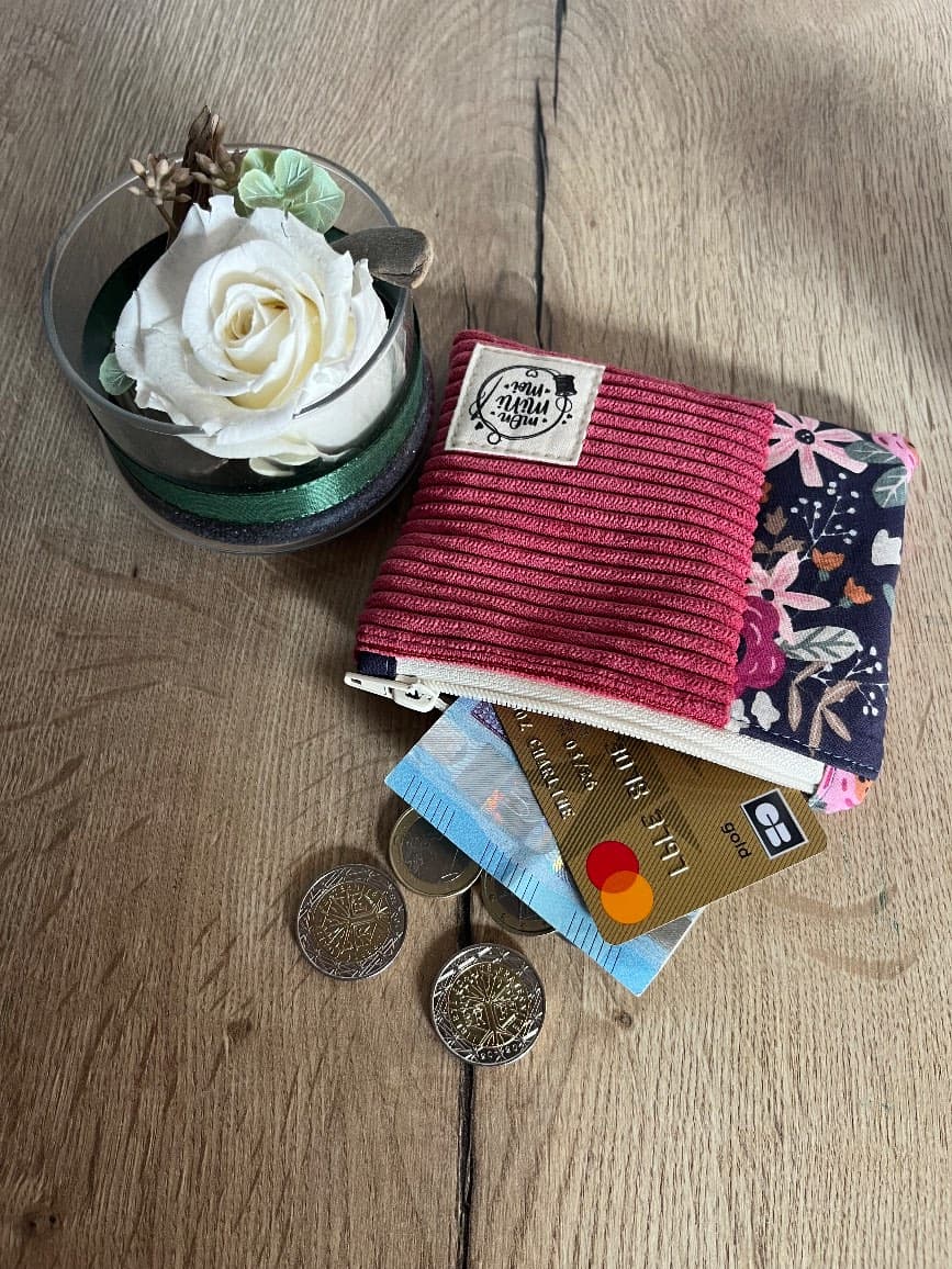 Vue du dessus du porte-monnaie bicolore avec pièces et carte bancaire qui dépassent.