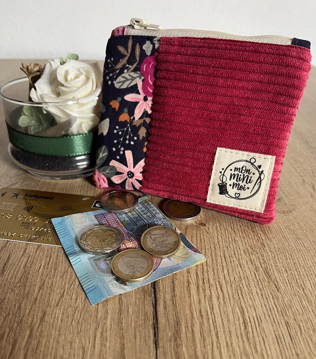 Porte-monnaie zippé en velours côtelé framboise et tissu fleuri posé avec monnaie et carte.