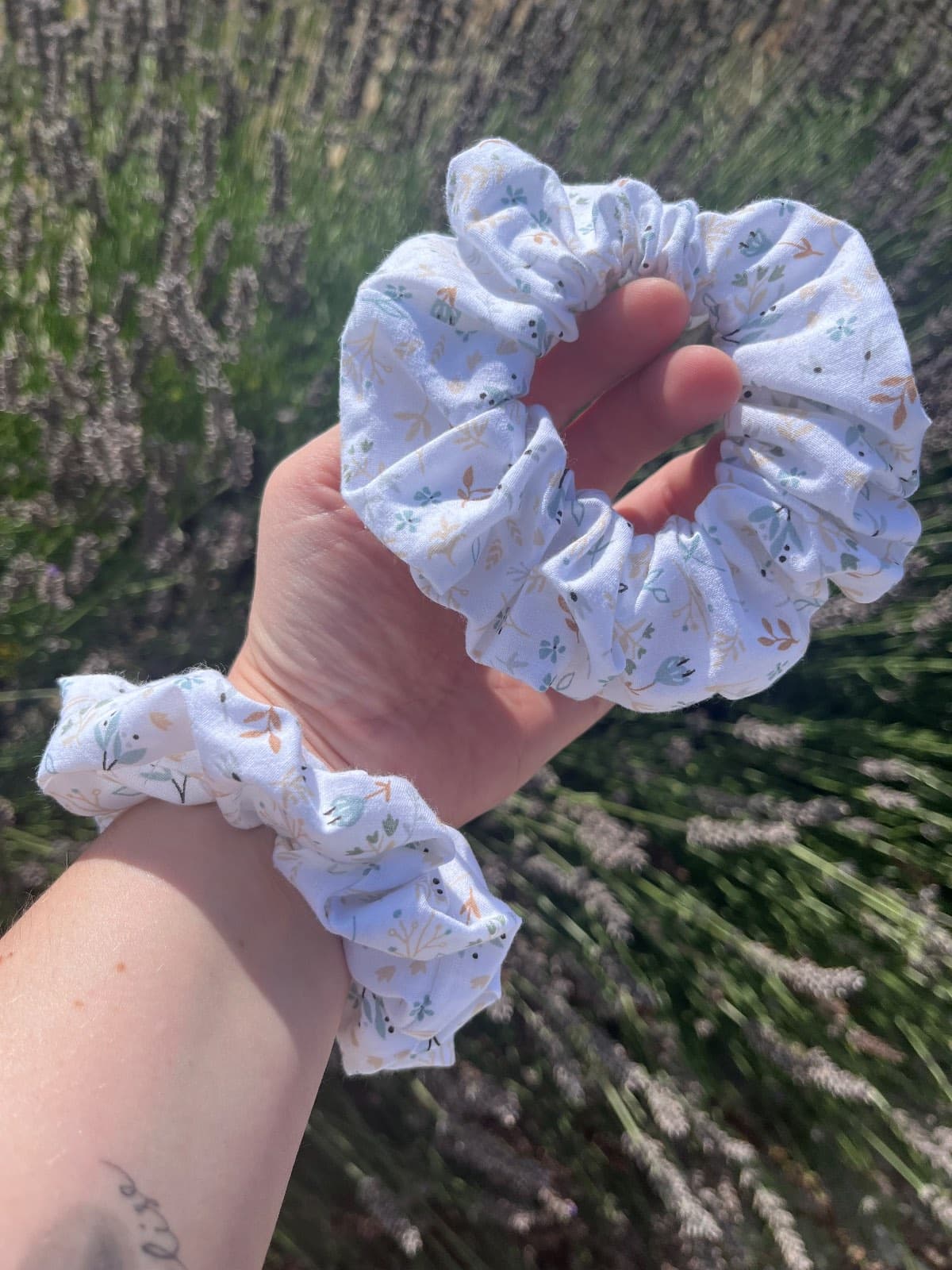 Chouchou blanc à motifs de feuilles douces porté au poignet et tenu en main.