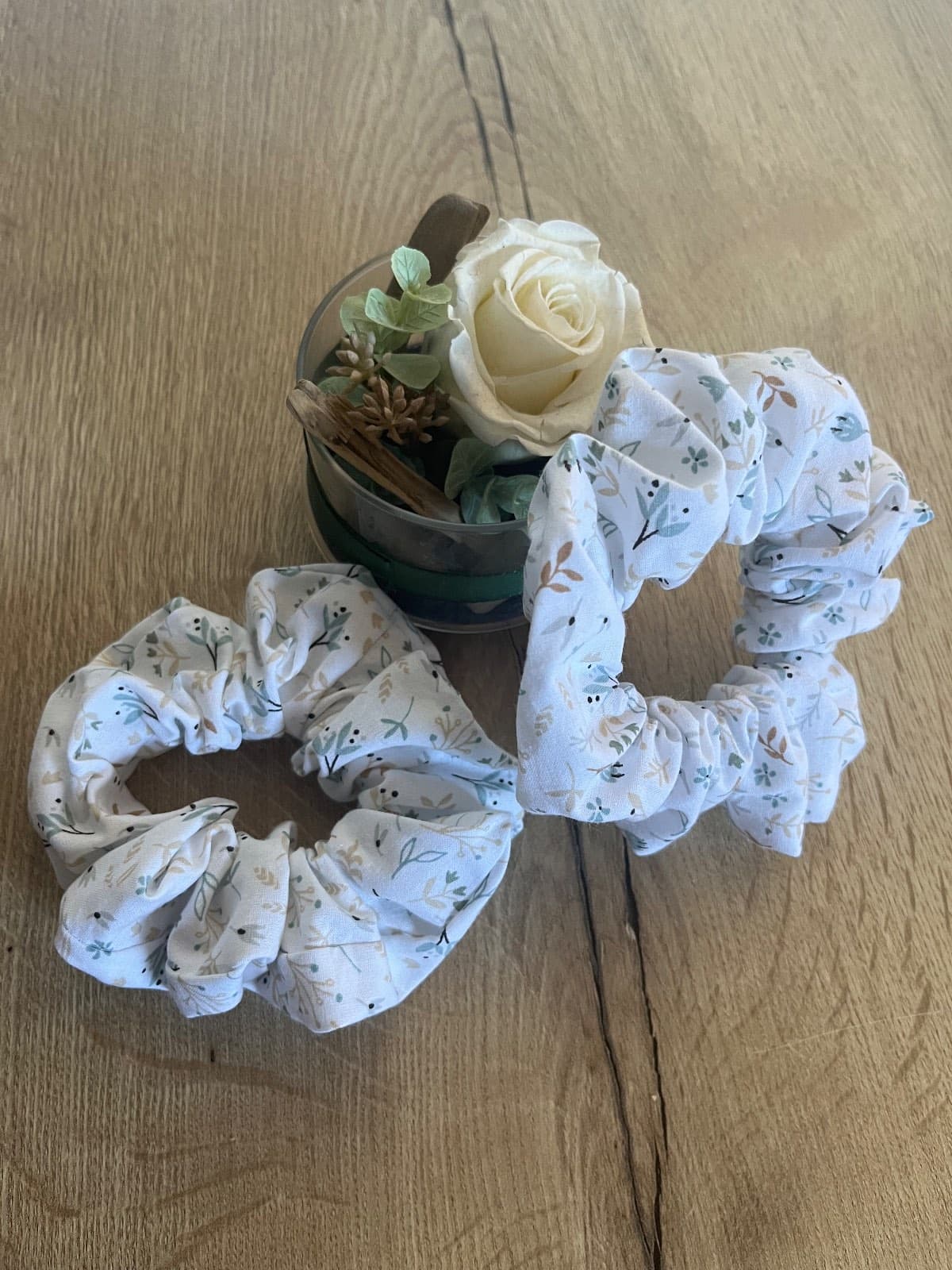 Deux chouchous froncés à motif végétal délicat sur tissu clair posés sur une table en bois.