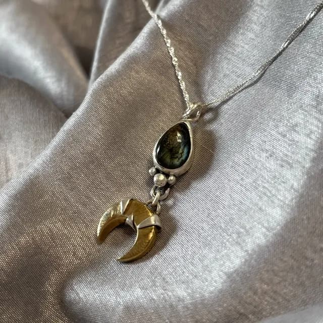 Gros plan sur le pendentif Lunae Lumen en argent et laiton avec reflets sur la pierre de labradorite.