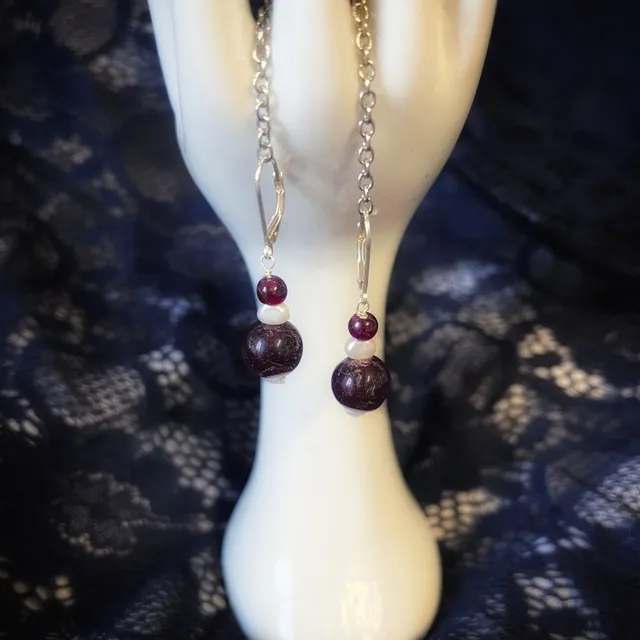 Paire de boucles d'oreilles dormeuses suspendues à un présentoir en forme de main blanche.