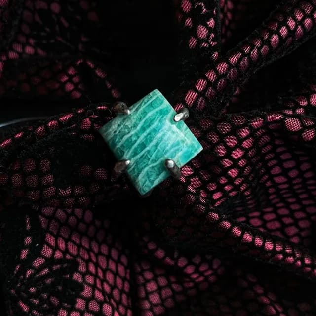Gros plan sur une pierre d'amazonite carrée bleu-vert sertie de quatre griffes en argent sur tissu noir.