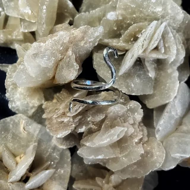 Bague spiralée argentée à l'effet martelé posée sur une roche minérale cristallisée.