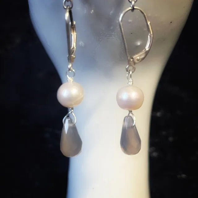 Boucles d'oreilles pendantes Arista avec perles naturelles présentées sur un porte-bijou en forme de main.