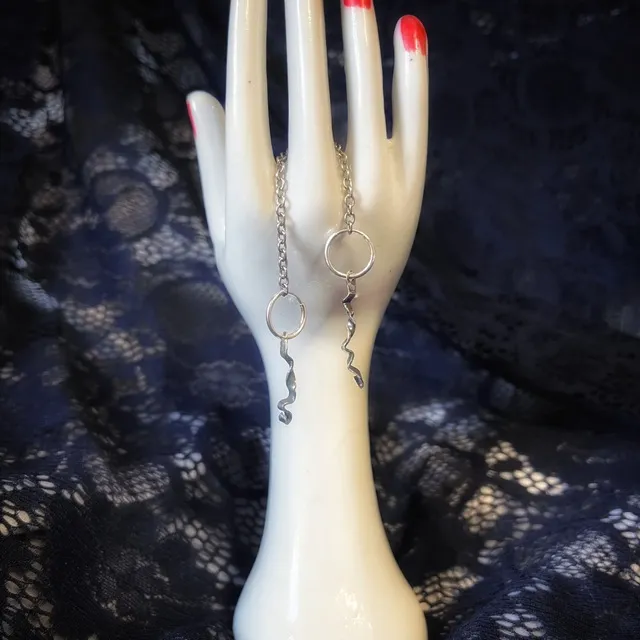 Créoles en argent et breloques torsadées suspendues à une main en porcelaine blanche.