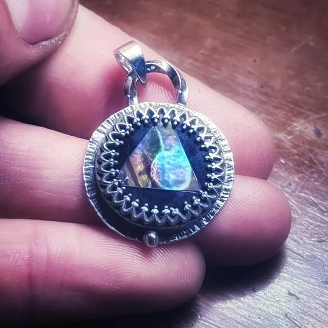Gros plan du pendentif médaillon tenu en main révélant les reflets irisés