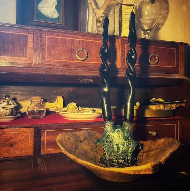 Vue d'ensemble du bougeoir rituel aux bougies torsadées noires posé sur un meuble en bois ancien.
