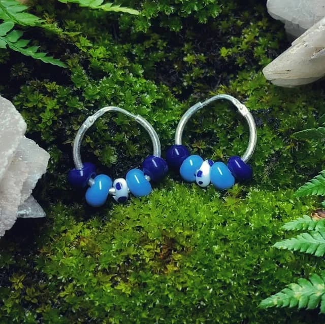Créoles en argent ornées de perles de verre bleues et blanches, posées sur de la mousse végétale.